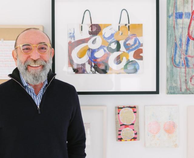 Photograph of Dani Levinas smiling in front of a wall of artwork
