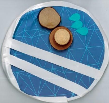 Circle with collage of white stripes, three tear drops, and wood chips.