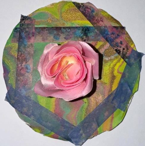 Circle with collage of a pink flower on abstract, blue and yellow paper.
