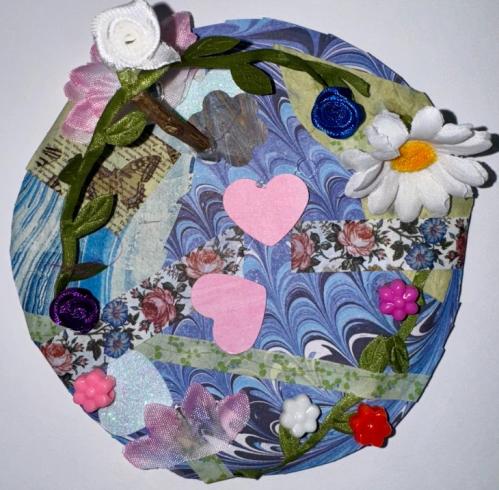 Circle with collage of flowers, leaves, and hearts on wavy, blue paper.