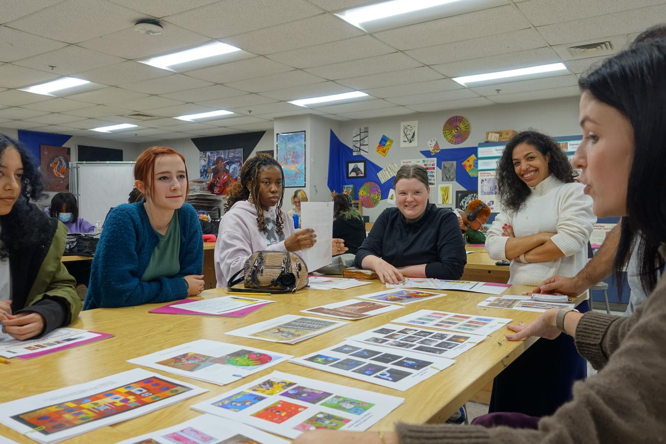 Group of students sitting around a table with images or artworks on the table