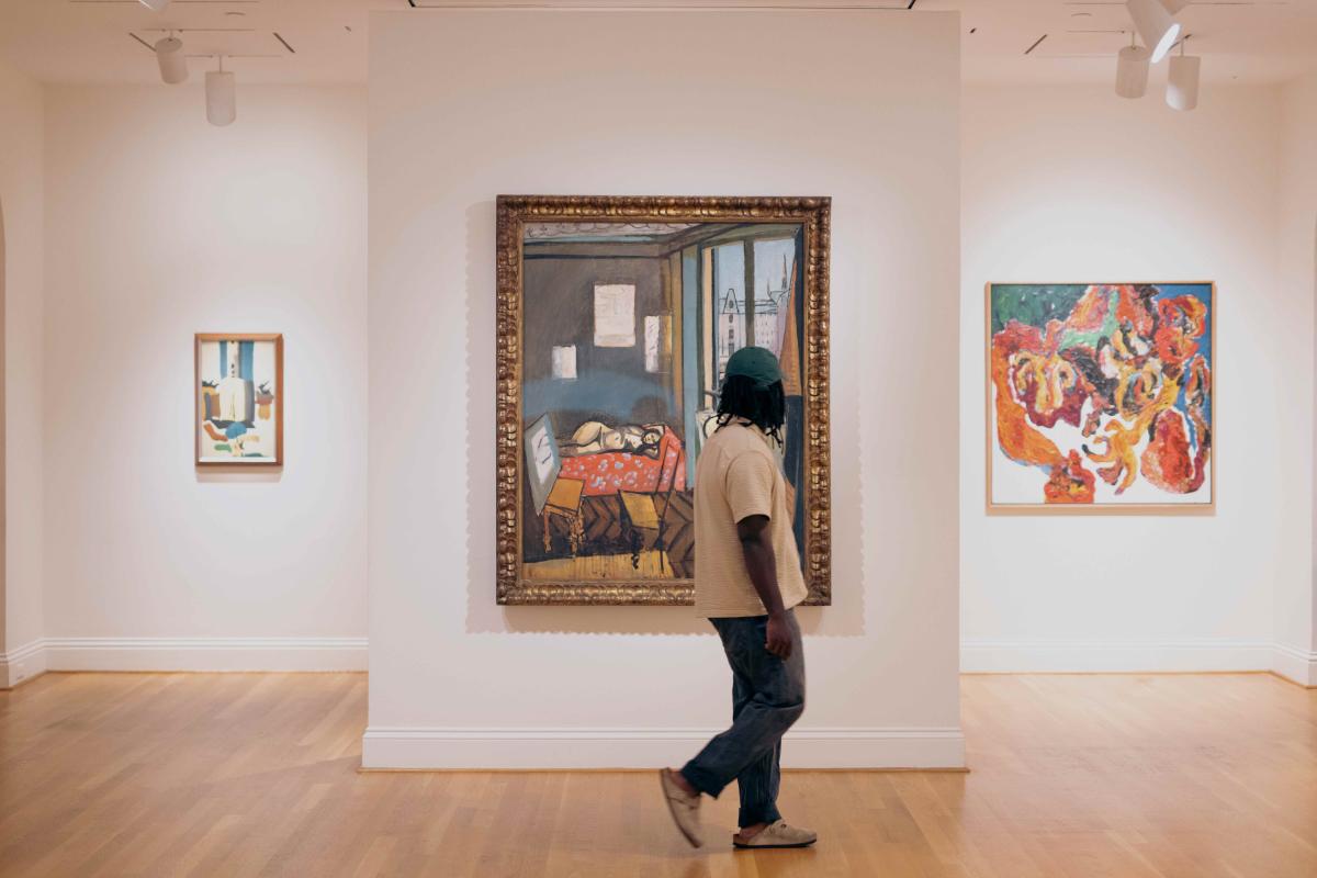 Man walking in front of three paintings in an art museum