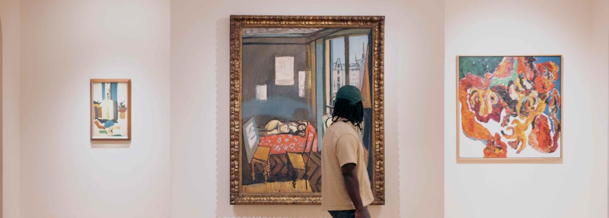 Man walking in front of three paintings in an art museum