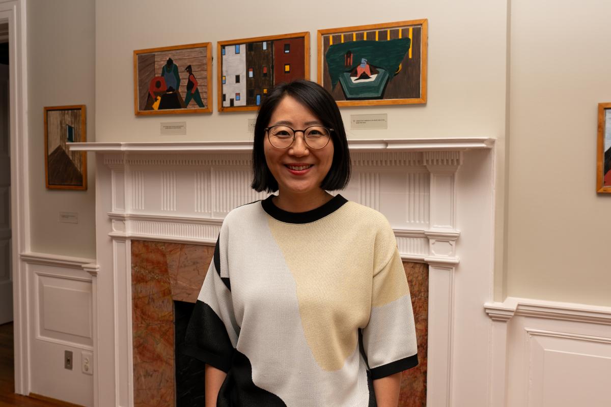 A woman standing in front of a fireplace with paintings hanging above the mantle