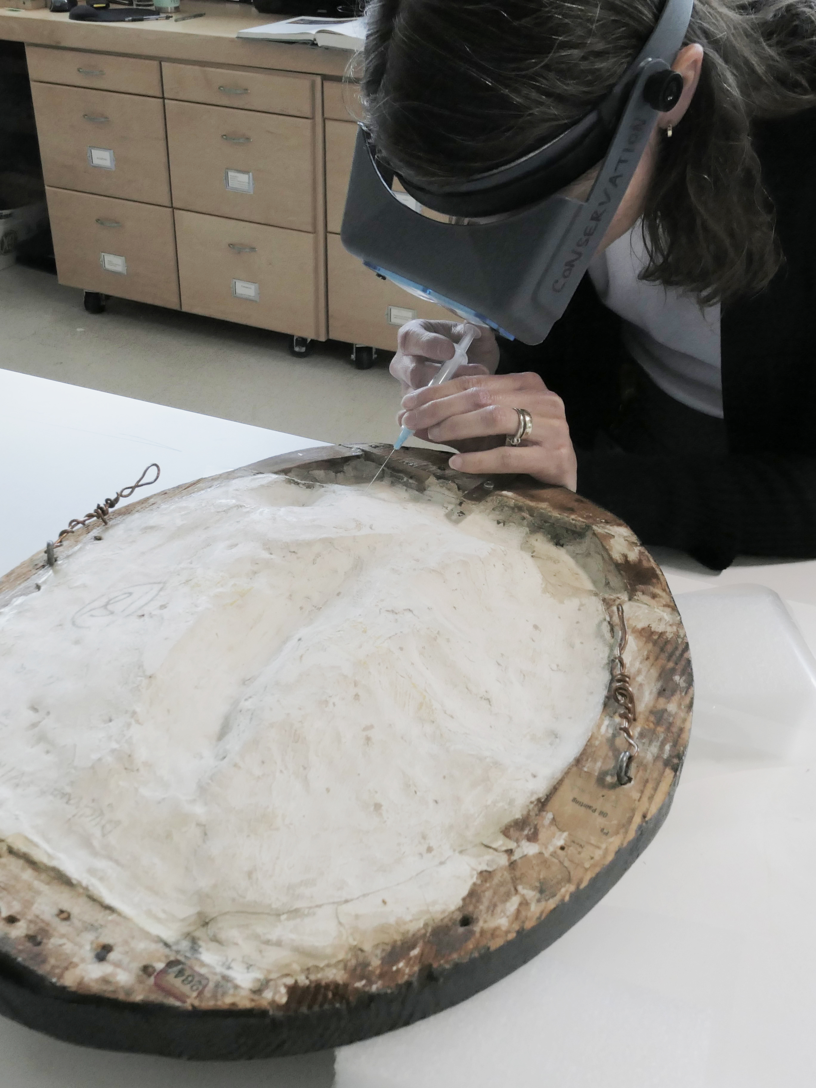 Photograph of a person using a syringe to inject adhesive into the back of Gallic Cock by Raymond Duchamp Villon 